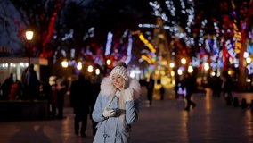 Portrait of young attractive girl in urban winter background listening to music with smartphone, New Year holidays, video in slow motion