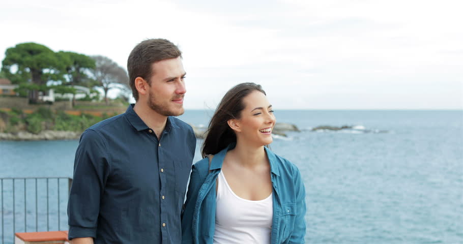 Happy couple walking on the beach talking and pointing horizon with the sea in the background