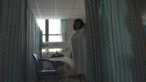 Woman in hospital gown closing cubicle curtain for privacy