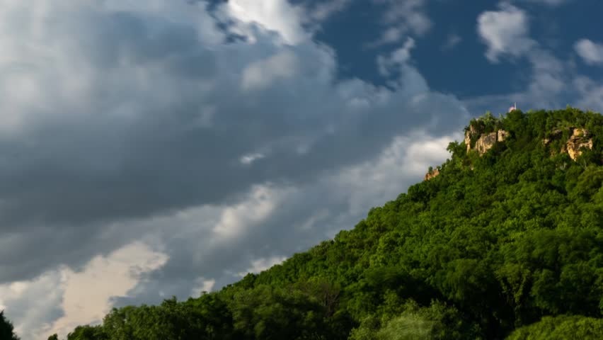 Time Lapse of Puffy clouds moving behind a bluff