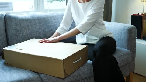 PARIS, FRANCE - CIRCA 2018: Elegant fashionable woman open unboxing new cardboard with multiple clothes shoes on the living room sofa - online shopping from Inditex Massimo Dutti
