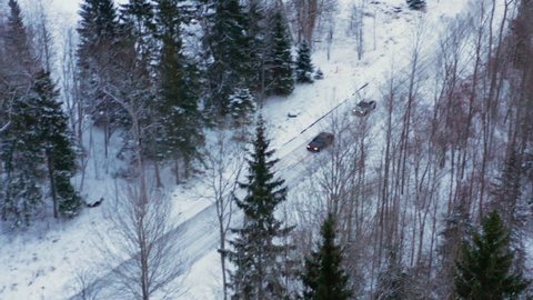 Overhead aerial tracking shot of two cars drifting and racing on snowy road. Aerial shot of vehicles racing on narrow and icy winter road in forest