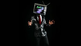 Cool male performer in silver tuxedo jacket dancing with a television as a head. There is distortion and static on the TV screen