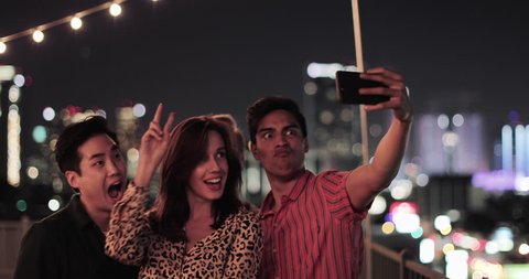 Group of friends taking selfies with city skyline at night