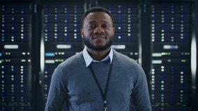 Bearded Black IT Engineer Standing and Posing with Crossed Arms in the Middle of a Working Data Center Server Room with Server Computers Working on a Rack. - Powered by Shutterstock - Get 15% off with code: PIKWIZARD15