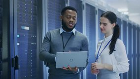 Black IT Technician with a Laptop Computer Gives a Tour to a Young Intern. They Talk in Data Center while Walking Next to Server Racks. Running Diagnostics or Doing Maintenance Work. - Powered by Shutterstock - Get 15% off with code: PIKWIZARD15