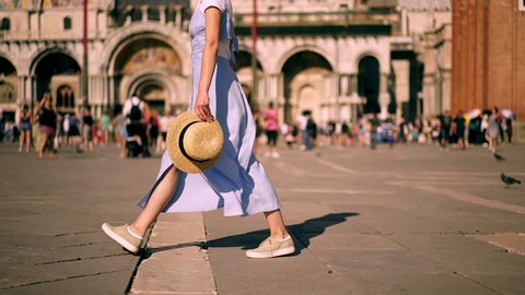 Slow motion effect of carefree female tourist with smartphone device and hat in hands feeling good walking at old town square. hipster girl turning around enjoying summer vacation holidays in Venice