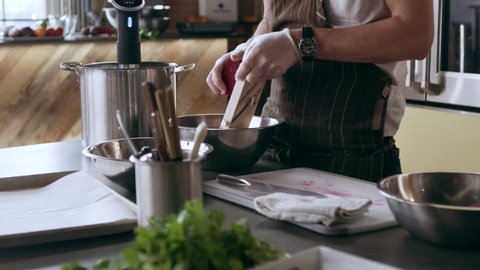 Professional chef grating beets with a mandolin into a bowl while other chefs are working in interior kitchen with soft day lighting. Medium close up to Wide shot on 4k RED camera on a gimbal.