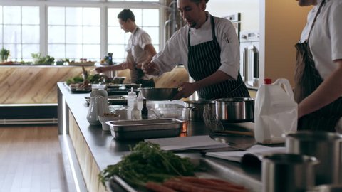 Three professional chefs cooking and preparing food in pots and pans in interior kitchen with soft day lighting. Medium shot on 4k RED camera on a gimbal in slow motion.
