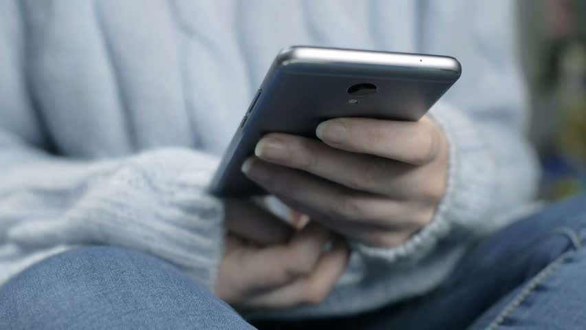 Young girl in blue pastel sweater hold smartphone in hand. Close up slow motion footage.