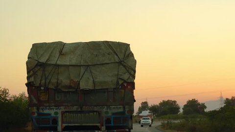 Silhouette of truck driving on a highway at dusk in india. Shot from a car following the truck with other cars coming from the opposite direction. highways and trucks form the backbone of the indian