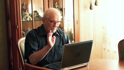 Senior man chatting on laptop by table at home
