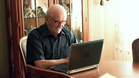 Senior man chatting on laptop by table at home

