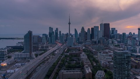 The historic and modern Toronto city skyline with car traffic travelling down the Gardiner Expressway to and from downtown Toronto during a beautiful moody sunset at night. 