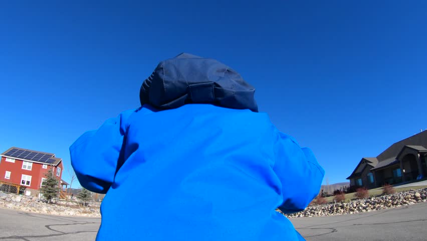 A slow motion shot of a little boy riding his bike on a cold day with his mittens