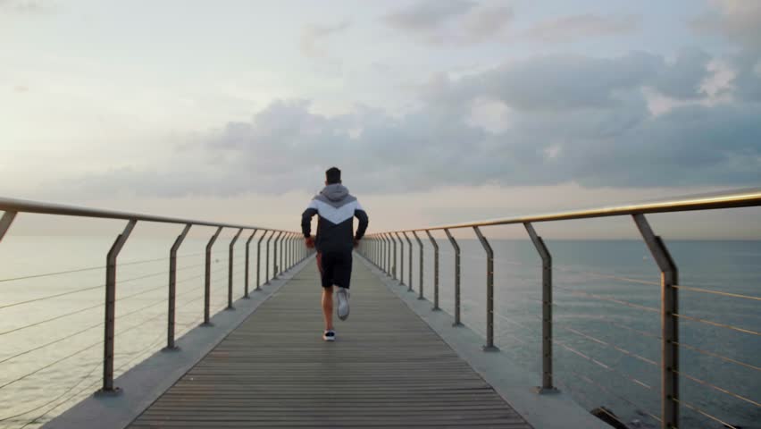 Young attractive athlete running away on a Bridge in the morning from a perspective point of view in slow motion. | Shutterstock HD Video #1022001424