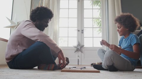 Side view of a mixed race pre teen boy and his middle aged black father sitting cross legged opposite each other on the floor playing an educational game, low angle, close up