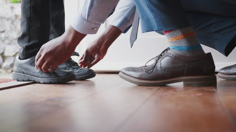 Close up of father wearing shirt and tie, brogue shoes and striped socks kneeling down on one knee to fasten the straps on his sons shoes before school, low section, close up of feet