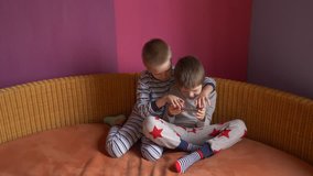 Funny kids lay on sofa to play computer games on smartphone. Parents gave the children a new phone for Christmas. Modern children are well aware of latest technology. Brothers are happy together