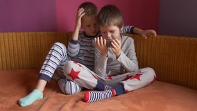 Funny kids lay on sofa to play computer games on smartphone. Parents gave the children a new phone for Christmas. Modern children are well aware of latest technology. Brothers are happy together