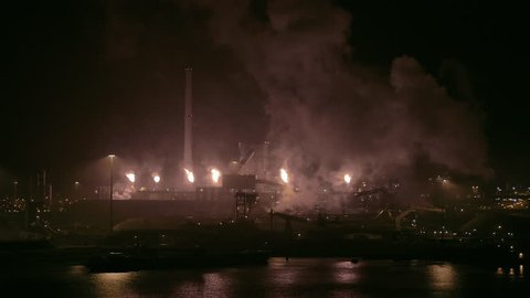 AERIAL - A drone moves sideways and shows an industrial old factory working with big flames and a lot of smoke on the middle of the night.
