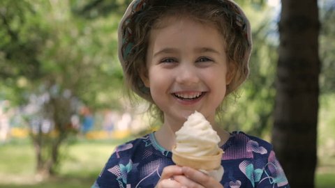 A cute little girl enjoys a delicious ice cream cone during the summer. Child with ice cream on a walk in the city park