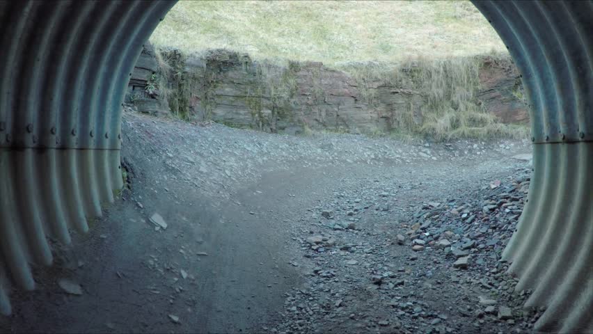 Two mountain bikers cycle through large underground tube at end of trail