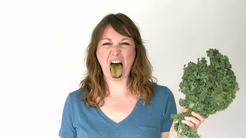 woman in studio eats kale raw and does not seem to like it at all.