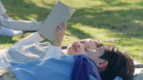 beautiful little asian girl and boy sister and brother lying on grass reading a book together in park