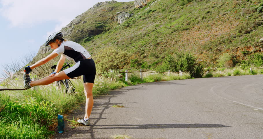 Middle age woman stretching on country road. Sky and mountain in background 