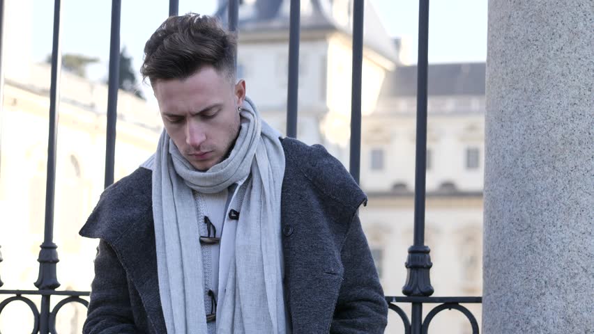 Portrait of young attractive man in winter coat using cell phone to take selfie photo outdoor in European city, Turin, Italy