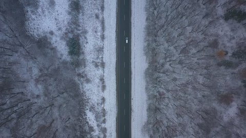 Aerial view of traffic on the road passing through the winter forest in blizzard