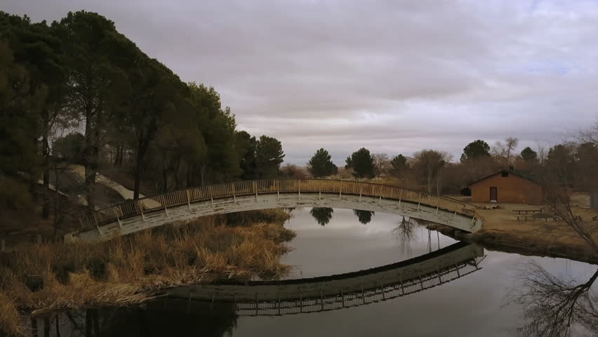Aerial reveal of Mojave Desert beyond a lovely lake bridge in Apollo Park, California