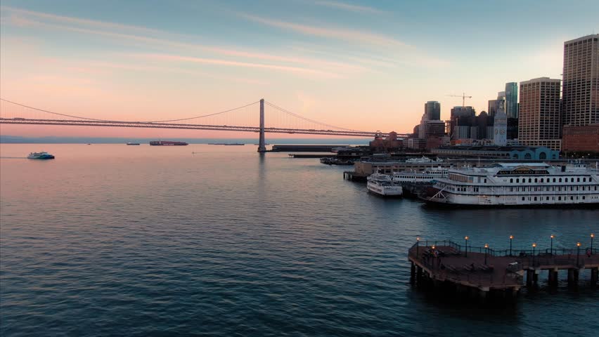 Aerial: San Francisco Embarcadero, the harbour & tourists walking on Pier 7 at sunset.