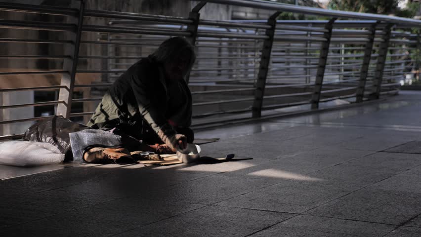 Homeless old man in dirty clothes sitting on the street and asking for help