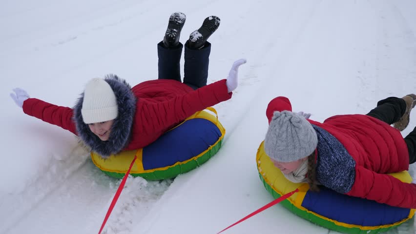 Happy children ride snow on snowy road and laugh with pleasure. Girls sledding in winter and smiling. Cheerful girlfriends play in winter in nature. | Shutterstock HD Video #1022067376