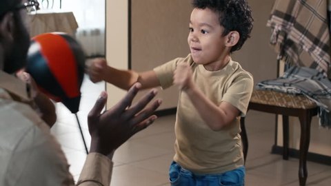 Over-the-shoulder shot of father training his son to fight with small punching bag at home