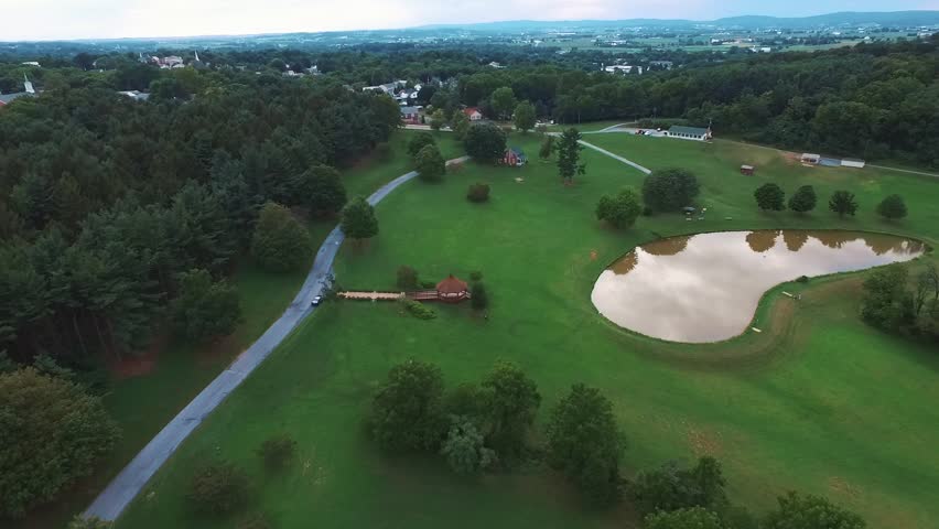 Aerial view of a big fishing pond in a park of Akron, Pennsylvania. Camera descending towards the pond.
