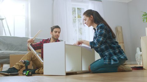 Happy Couple Assembles Furniture as a Team, Girl Reads Instructions and Boy Tightens Screw with a Drill. After Job is Done they do High Five. Moving into New Apartment, Couple Assemble Shelf.