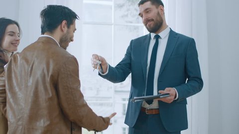 Professional Real Estate Agent Shows Bright New Apartment to a Young Couple. Successful Young Couple Becoming Homeowners, Seal the Deal with Real Estate Broker by Handshake. 