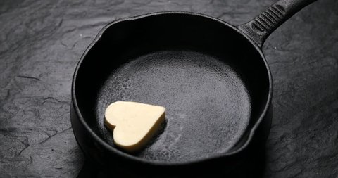 Fried butter, a piece of butter in the shape of hearts, fried on a black cast-iron pan. Impression about a healthy heart, anti cholesterol prophylaxis, healthy heart concept, 4k