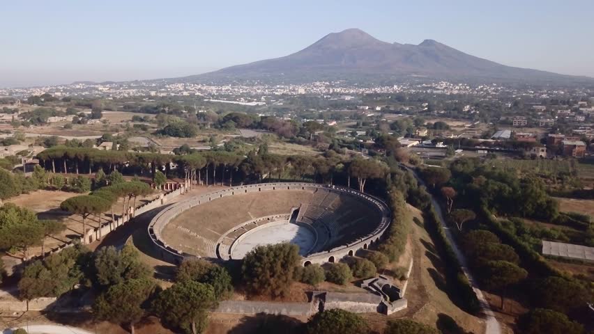 The ruins of a Roman amphitheater in Pompeii overshadow by Mount Vesuvius Royalty-Free Stock Footage #1022090440