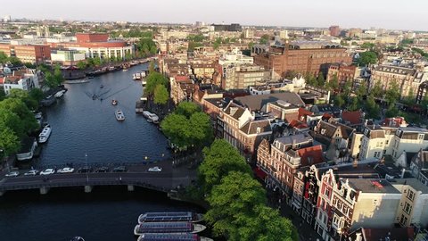 Amsterdam, Netherlands, aerial view of famous places during sunset in spring or summer.  Flying above canal and old centre district. Munttoren Bell Tower in background. Beautiful warm colors