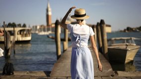 Slow motion effect of positive carefree female tourist running on pier for making video of floating gondola and boats on Venice Grand canal, happy hipster girl enjoying summer vacations in Italy