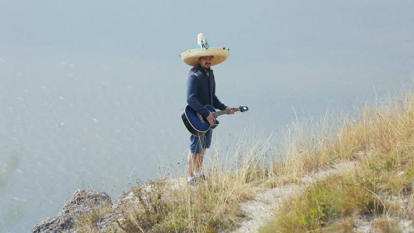 Mexican man mariachi playing acoustic guitar and singing at outdoors over a beautiful large lake.