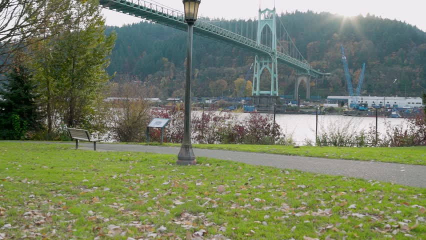 Slow motion wide dolly view of suspension bridge seen through a grassy park.