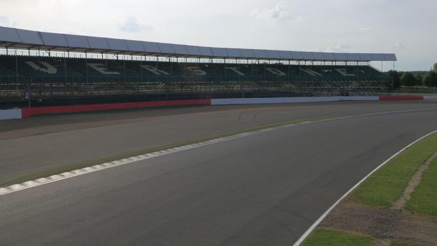 Two cars driving around fast corner at race track with pits in the background