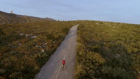 Aerial drone video of cyclist in white helmet and casual clothing ride up and down winding beautiful mountain road during warm summer sunset. Reach for goal or success, achieve your dream concept