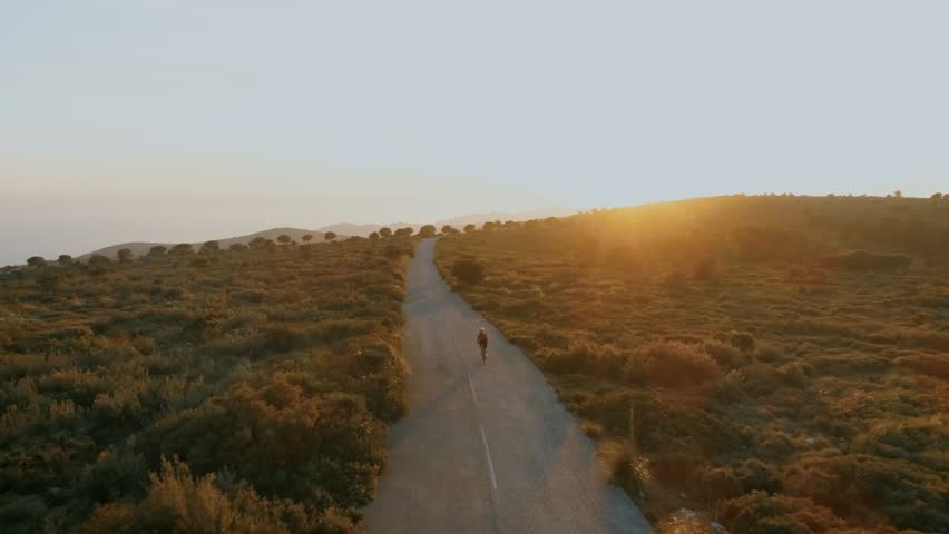 Sunset flare sun beam light in lens of aerial drone footage of young female woman on road bicycle ride up winding mountain pass. Epic and motivational landscape or concept for training or sports | Shutterstock HD Video #1022101726