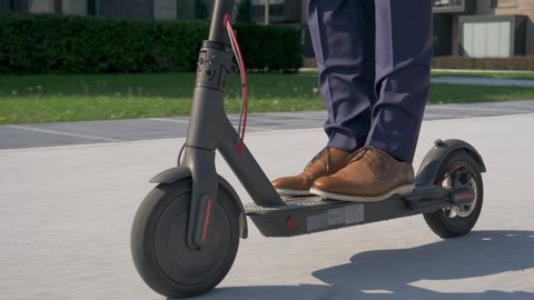 Close up - Adult male in business attire riding with electric scooter to work